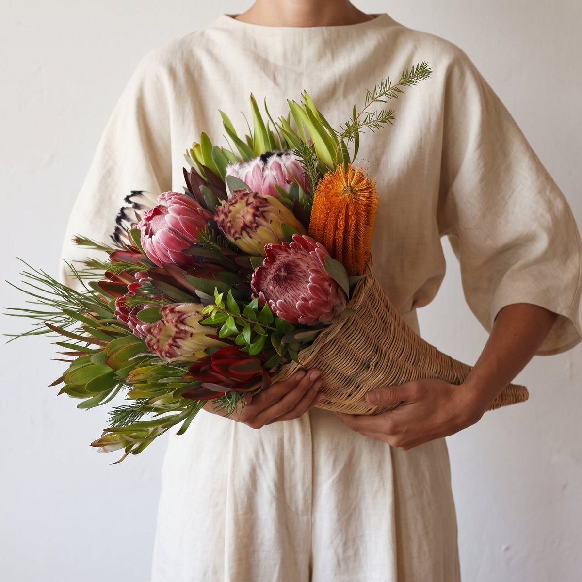 Woman in linen clothing holding a thanksgiving protea bouquet with a cornucopia
