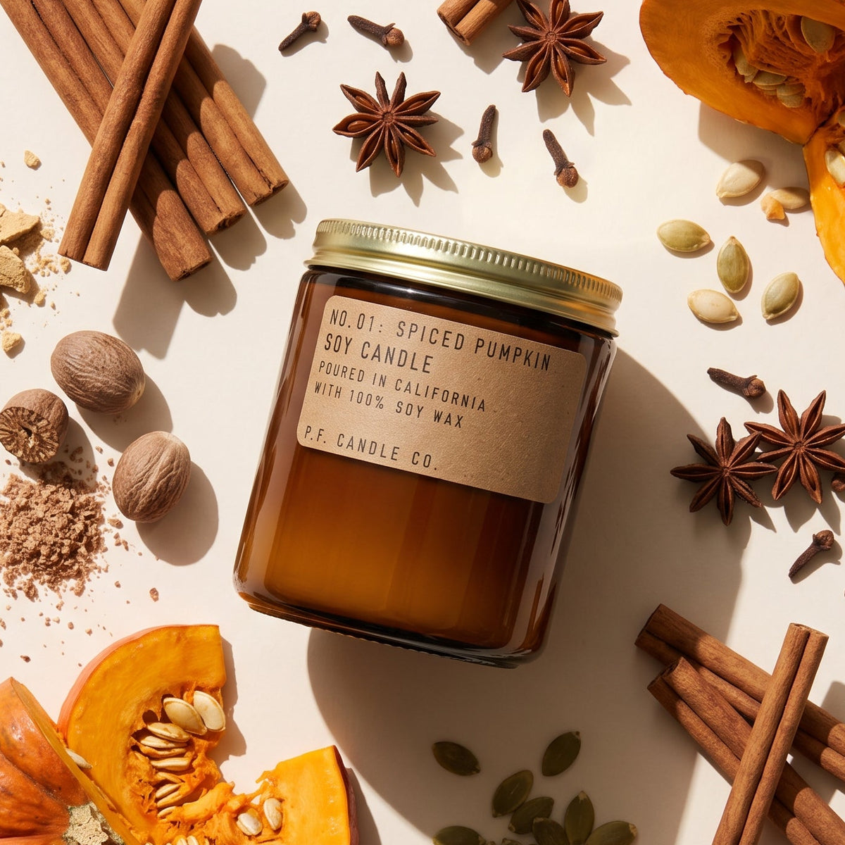 Pumpkin spice candle surrounded by pumpkin, cinnamon, nutmeg and other ingredients