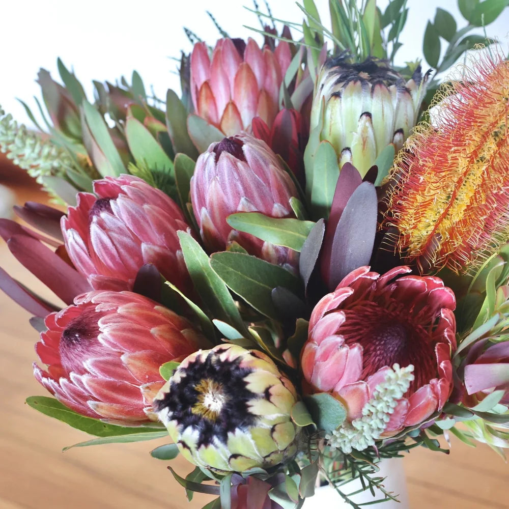 Bouquet of protea flowers with greenery on a wooden surface